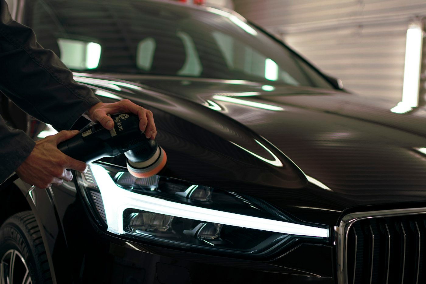 Detailer machine polishing the paint of a black car in a workshop